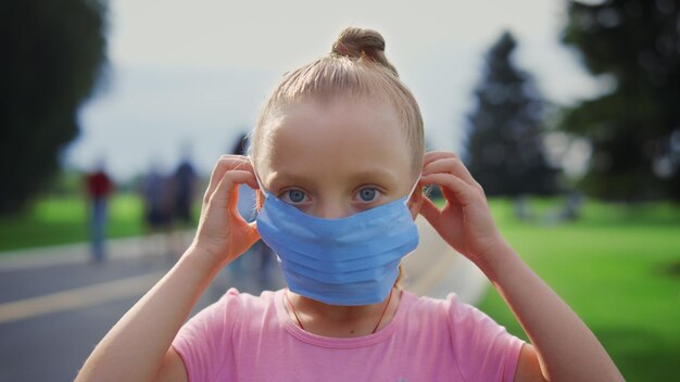 Retrato de una chica hermosa mirando a la cámara con una máscara médica en el parque de la ciudad