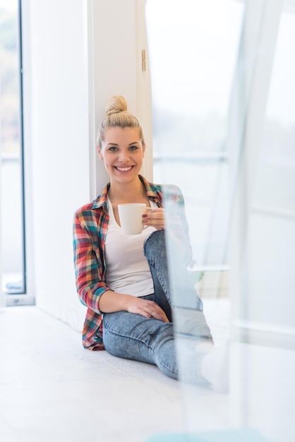 Retrato de una chica hermosa que está sentada en el suelo y bebiendo café