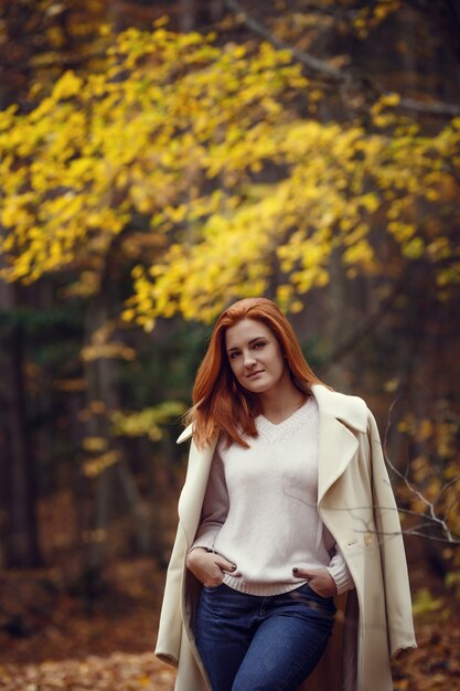 Retrato de una chica hermosa, soñadora y triste con el pelo rojo en otoño de bata blanca