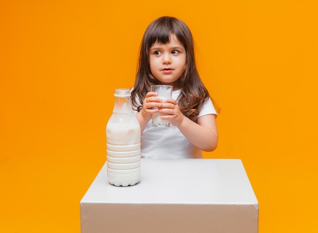 Foto retrato de una chica hermosa con un vaso de leche sobre fondo amarillo