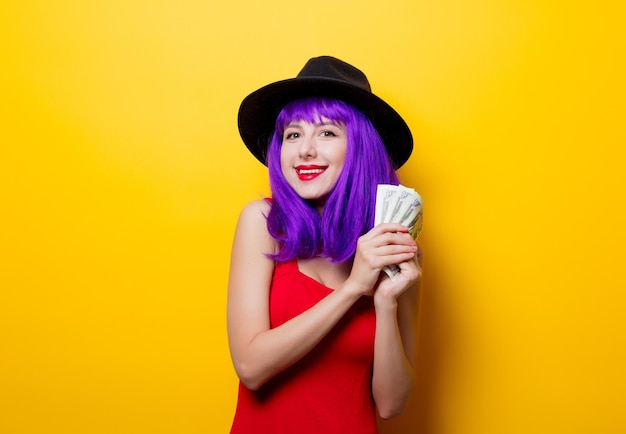 Retrato de chica hipster de estilo joven con peinado morado con dinero sobre fondo amarillo