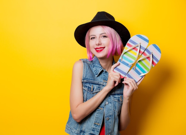 Retrato de chica hipster de estilo joven con peinado rosa y zapatos de chanclas sobre fondo amarillo