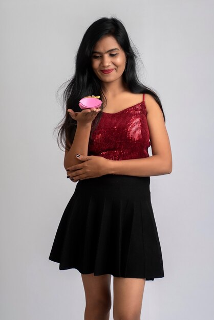 Retrato de una chica joven y bonita posando con caja de regalo en gris.