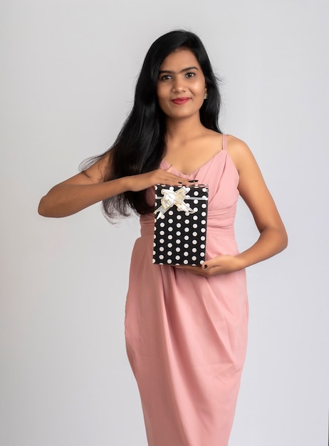 Foto retrato de una chica joven y bonita posando con caja de regalo en gris.