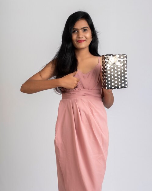 Retrato de una chica joven y bonita posando con caja de regalo en gris.