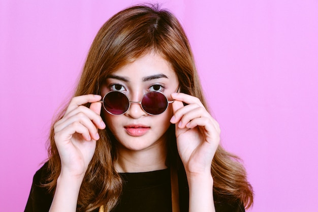 Retrato de la chica joven con las gafas de sol en fondo rosado