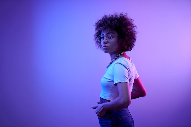 Retrato de una chica kazaja genial con rizos y tatuajes posando en luz de neón aislada en el fondo del estudio