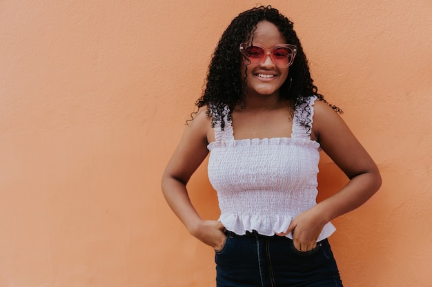 Retrato de una chica latina con gafas de sol delante de una pared.