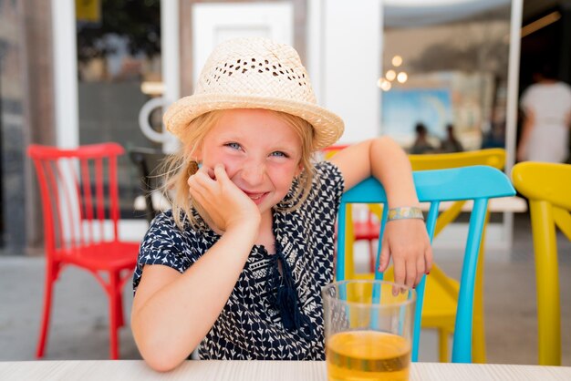 Retrato de una chica linda con sombrero sentada en un restaurante al aire libre