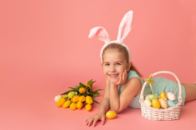 Retrato de una chica linda y sonriente con orejas de conejo y huevos de Pascua cerca de un ramo de tulipanes de primavera