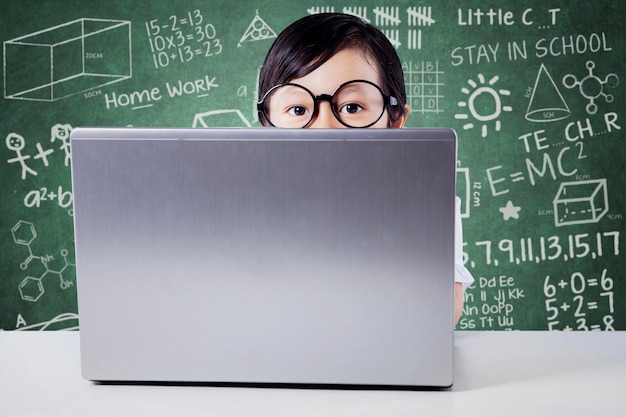 Retrato de una chica linda usando una computadora portátil en la mesa contra el tablero