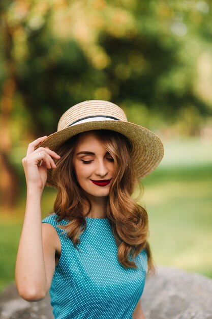 Retrato de una chica de moda con un vestido azul y elegante sombrero en el parque.