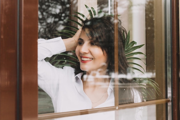 Retrato de una chica morena de pie detrás de una puerta de cristal.