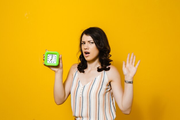 Foto retrato de una chica morena que está desesperada por una alarma diaria en una pared amarilla