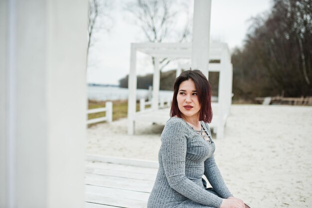 Retrato de una chica morena con vestido gris sentada en una construcción de madera blanca