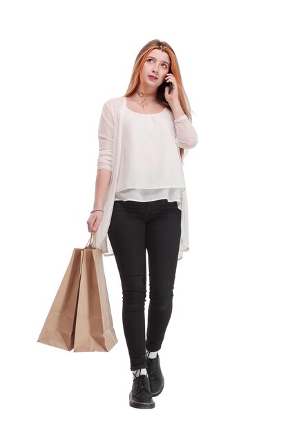 Retrato de una chica muy feliz hablando por teléfono móvil mientras sostiene bolsas de compras y mira hacia otro lado en el espacio de copia aislado sobre fondo blanco.