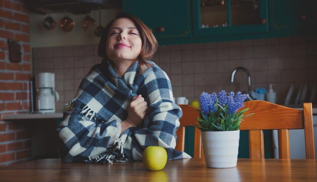 retrato de chica pelirroja a cuadros con manzana sentada a la mesa en la cocina.