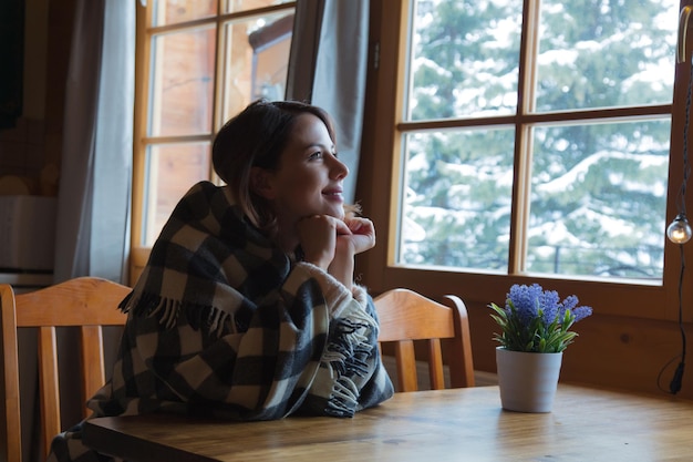 retrato de una chica pelirroja a cuadros sentada en la mesa en la cocina cerca de la ventana