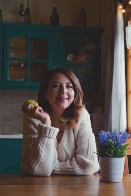 retrato de chica pelirroja con manzana sentada en la mesa en la cocina.