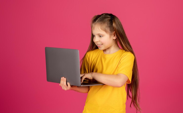 Foto retrato de una chica preadolescente curiosa usando una computadora portátil mientras está de pie sobre un fondo rosa