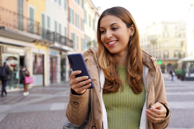 Retrato de una chica que envía mensajes al aire libre con una aplicación de chat en un teléfono inteligente en una zona peatonal