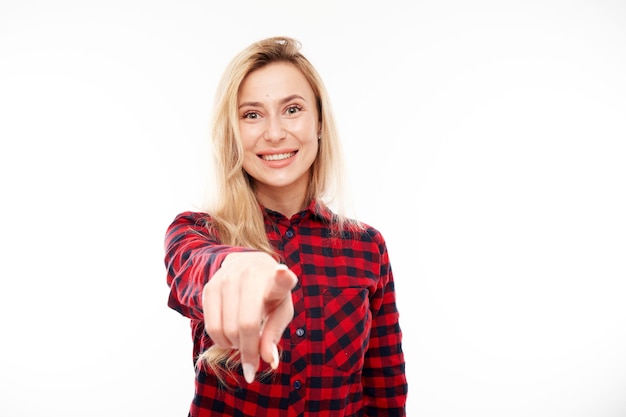 Retrato de una chica rubia amistosa que te elige apunta con el dedo a la cámara aislada de fondo blanco