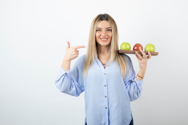 Retrato de una chica rubia apuntando a la tabla de madera con manzanas verdes y rojas