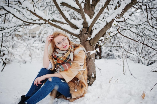 Retrato de chica rubia con gafas, abrigo de piel rojo y bufanda en el día de invierno.