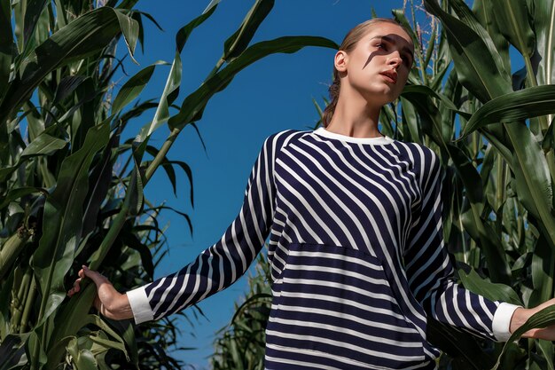 Retrato de una chica rubia en ropa de moda y con estilo, entre el follaje de un campo de maíz.