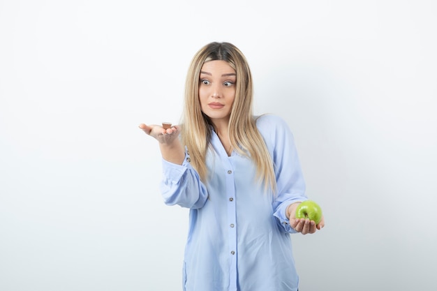 Retrato de una chica rubia sosteniendo manzana verde sobre pared blanca