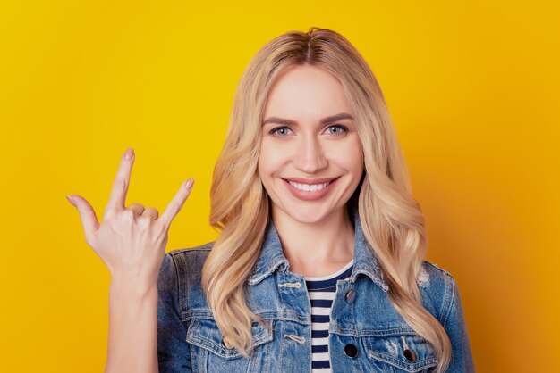 Retrato de chica ruda hipster fan mostrando cuernos gesto de rock and roll sobre fondo amarillo