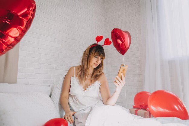 Retrato de una chica sexy en el dormitorio en el Día de San Valentín se toma una selfie en su teléfono inteligente. Dia de la mujer.