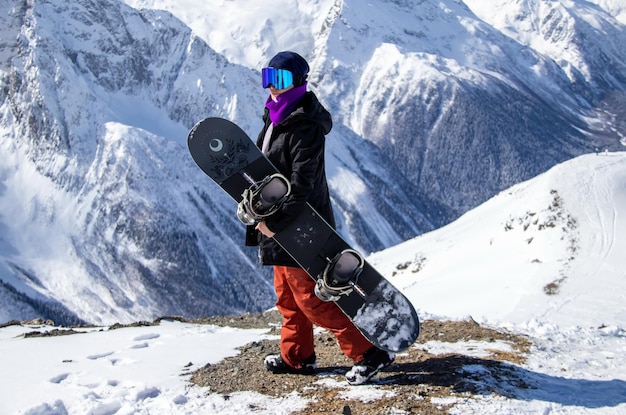 Retrato de una chica con snowboard en la cima de una montaña nevada.