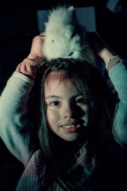 Foto retrato de una chica sonriente con un conejo en la cabeza