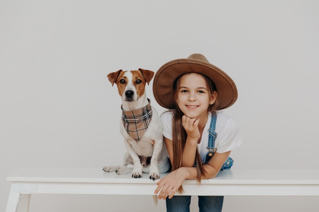 Foto retrato de una chica sonriente con un perro en la mesa contra un fondo blanco