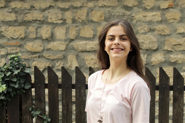 Retrato de una chica sonriente de pie contra una pared de piedra