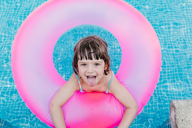 Retrato de una chica sonriente sacando la lengua en un anillo inflable en una piscina