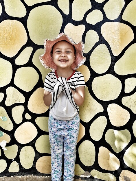 Foto retrato de una chica sonriente con sombrero de pie contra la pared
