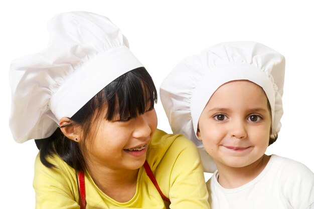 Foto retrato de una chica sonriente con su hermana con sombreros de chef contra un fondo blanco