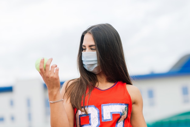 Retrato de chica tenista sosteniendo una pelota afuera con máscaras protectoras