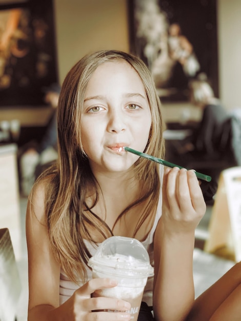 Foto retrato de una chica tomando café mientras está sentada en una cafetería