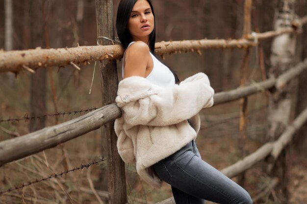 Retrato de una chica turista con una camisa blanca y jeans apoyados en una cerca de madera en un hermoso prado de otoño al atardecer