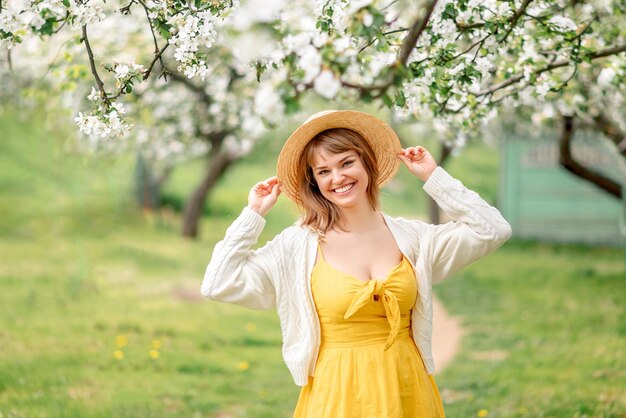 Retrato de una chica con un vestido amarillo en un jardín en flor Una joven con un sombrero trenzado sonríe en primavera.