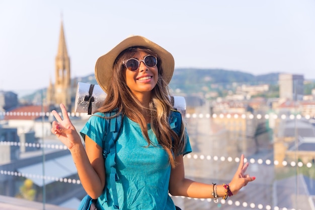 Retrato de chica viajera con mochila de viaje sonriendo y haciendo símbolo de paz