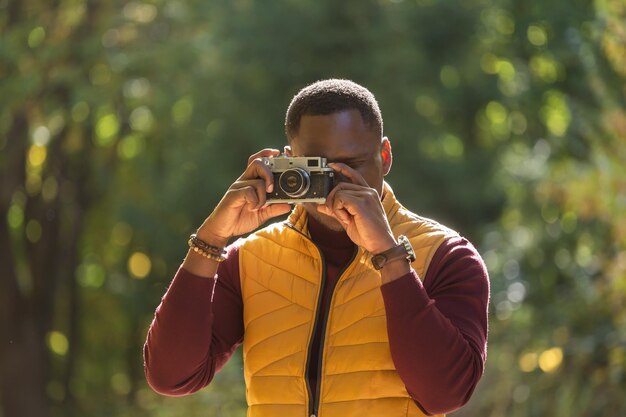 Retrato chico afroamericano fotógrafo tomando fotos con una cámara vintage en el parque verde de la ciudad diversidad de actividades de ocio y concepto de hobby