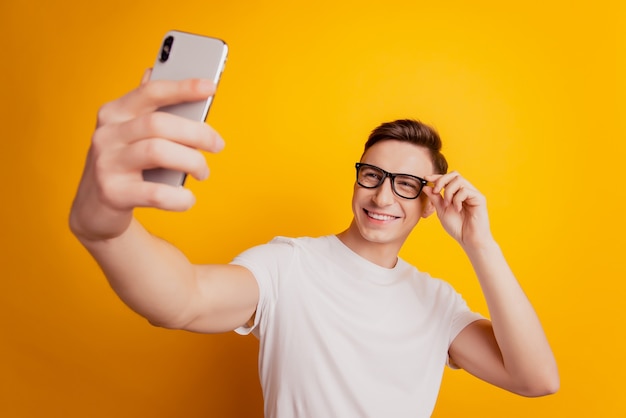 Retrato de chico alegre mantenga teléfono hacer selfie posando sobre fondo amarillo