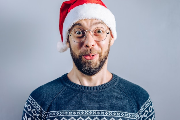 Retrato de un chico barbudo con gorro de Papá Noel y anteojos mirando asombrado