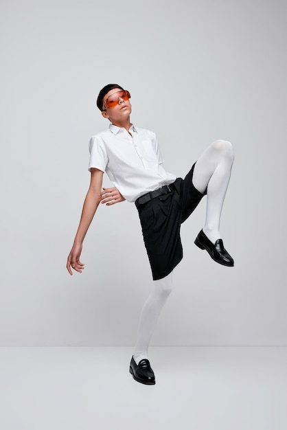 Retrato de chico elegante posando en pantalones cortos negros, camisa blanca y medias con gafas rojas aisladas sobre