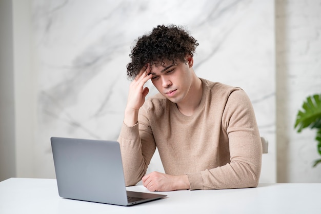 Retrato de chico guapo agotado cansado trabajando en equipo portátil joven guapo con exceso de trabajo es