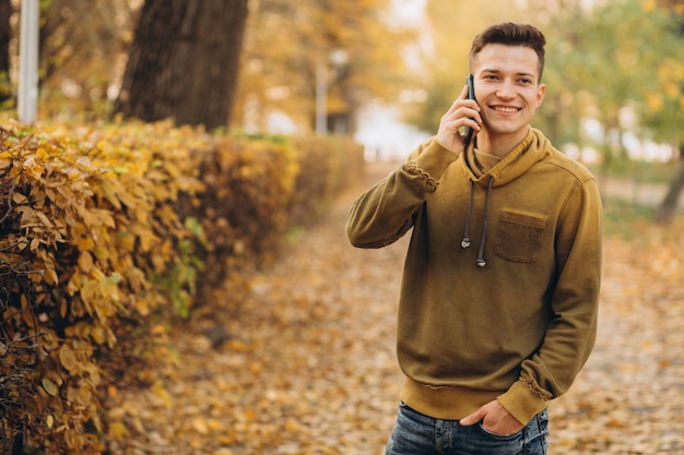 Retrato de chico guapo y feliz sonriendo y hablando por teléfono en el parque de otoño